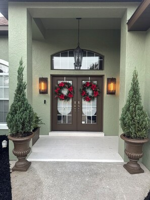 A front entrance with double doors, two potted evergreen trees, and two wall-mounted lanterns. - 3-bedroom house in beautiful Ocala with cool AC breeze (Ocala)