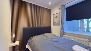 Un dormitorio moderno con cama, mesita de noche, ventana con vistas al exterior y pared con listones de madera verticales.
