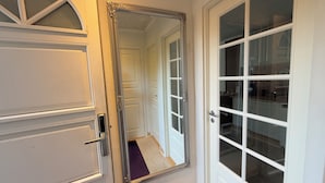 Un pasillo con un espejo grande que refleja una puerta y una ventana.