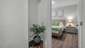 Ein Schlafzimmer mit Bett, Nachttisch, Lampe und einer Topfpflanze.