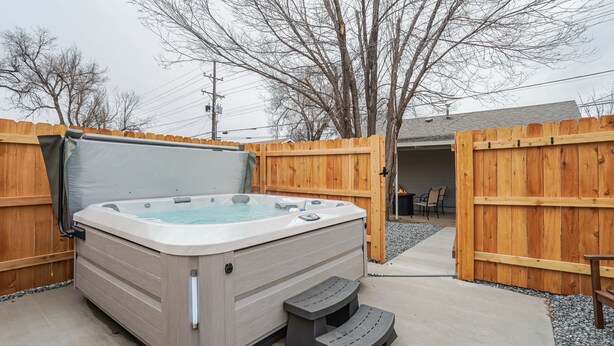 Un bain à remous dans un jardin, entouré de clôtures en bois, avec un patio couvert et un espace recouvert de gravier.