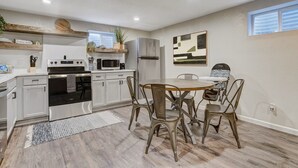 Une cuisine moderne avec des meubles blancs, un réfrigérateur en acier inoxydable et un coin repas comprenant une table en bois et des chaises en métal.