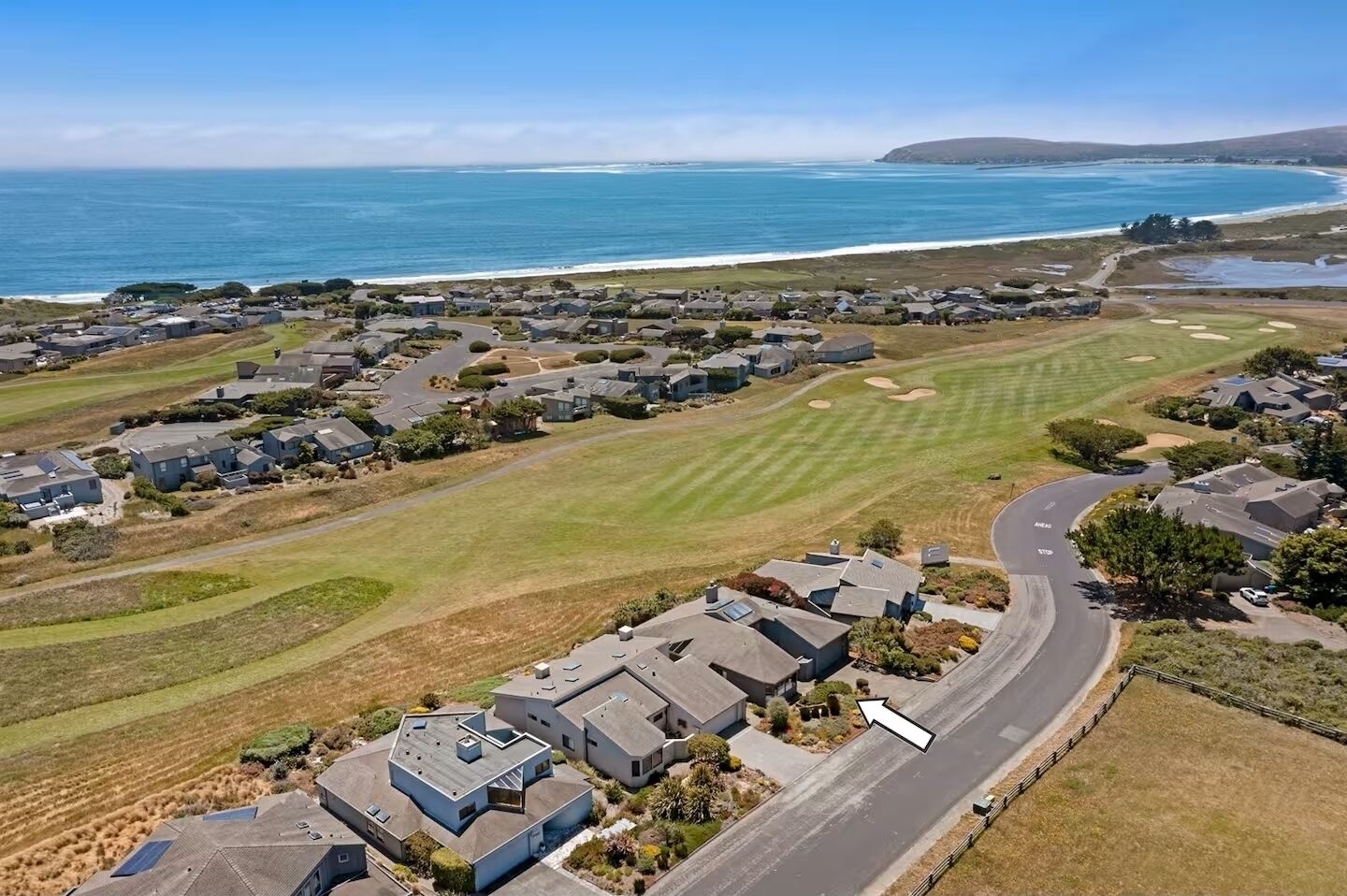 Vista aérea de una zona residencial costera con casas, un campo de golf y una carretera que serpentea por el paisaje.