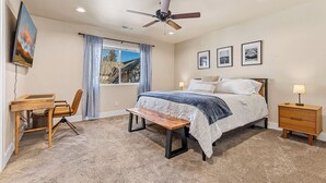 Quarto com cama, escrivaninha, cadeira, ventoinha no teto e janela com cortinas.