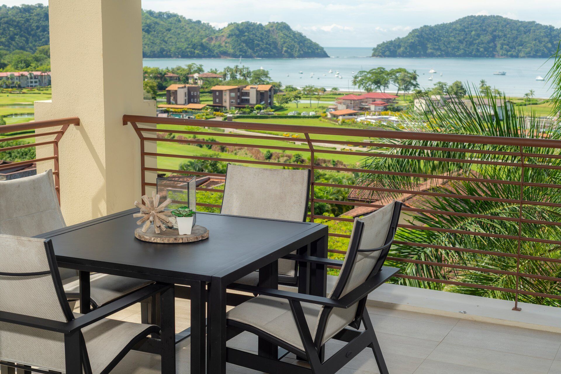 A balcony with a table and chairs, overlooking a scenic view of a lake and surrounding buildings.