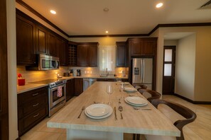 A modern kitchen with dark wood cabinets, stainless steel appliances, and a central island with dining setup. - AltaVista 4B 3 bdr Ocean View in Los Suenos (Herradura)