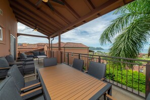 A covered outdoor seating area with a table and chairs, overlooking a residential neighborhood and a body of water. - AltaVista 4B 3 bdr Ocean View in Los Suenos (Herradura)