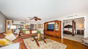 Una sala de estar con un sofá de cuero marrón, una mesa de centro de vidrio y un televisor sobre un mueble de madera.