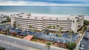 Un hotel de varios pisos con fachada curva, estacionamiento y vista al mar.