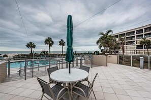 A rooftop pool area with a table and chairs, surrounded by palm trees and a view of the ocean. - Stunning 2+ St. Pete Beach condo directly on the sand. (St. Pete Beach)