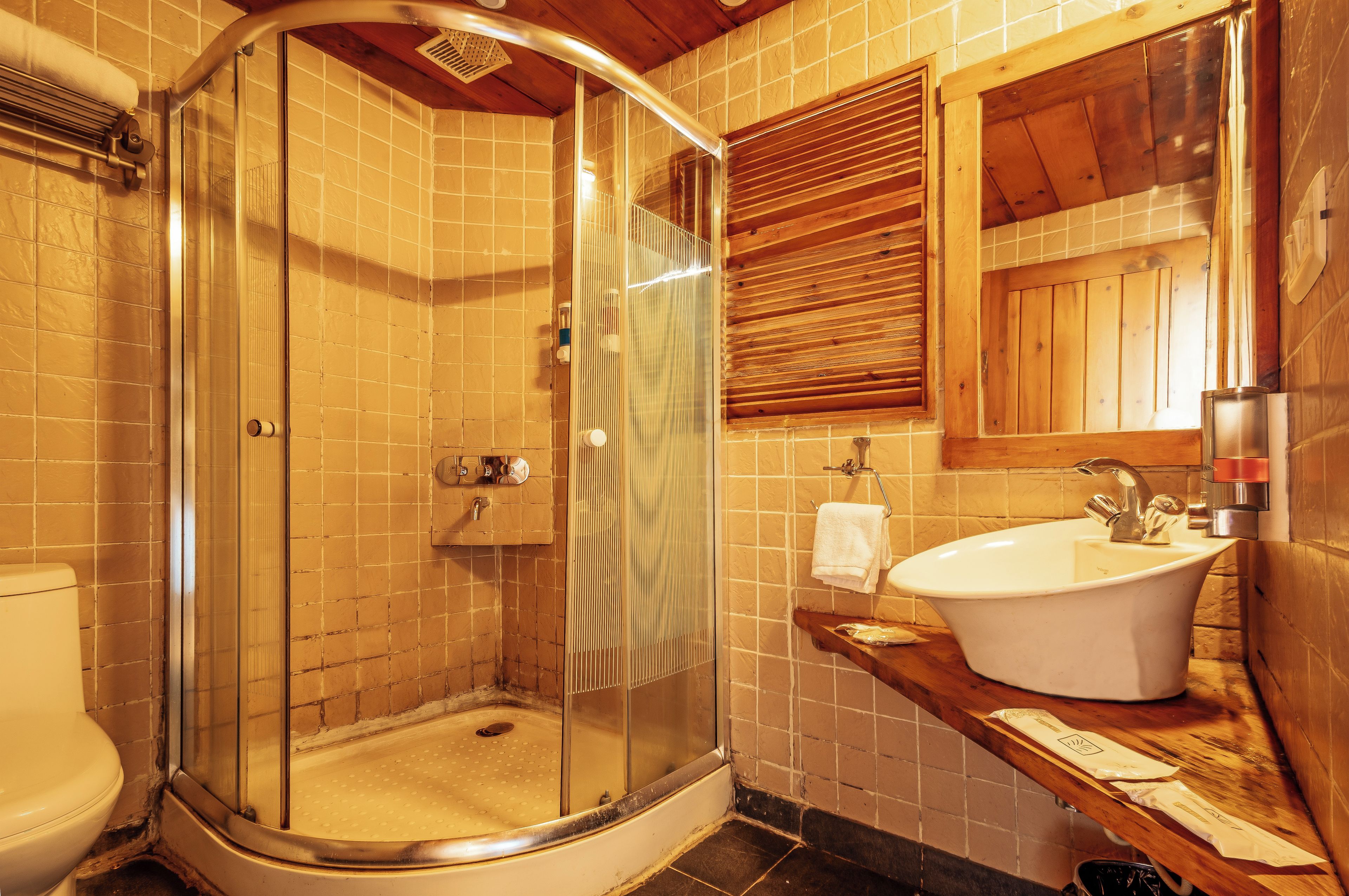 Un baño con ducha envuelta en vidrio, un lavamanos blanco y muebles de madera.