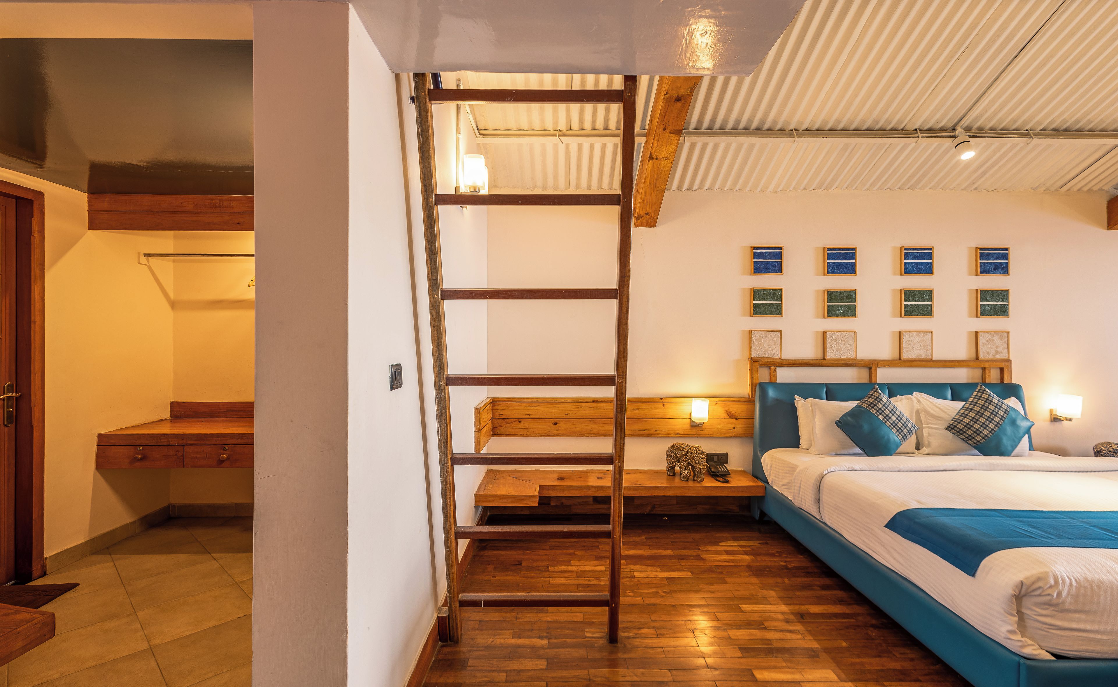 A bedroom with a bunk bed, wooden flooring, a headboard with multiple pillows, and wall-mounted artwork.