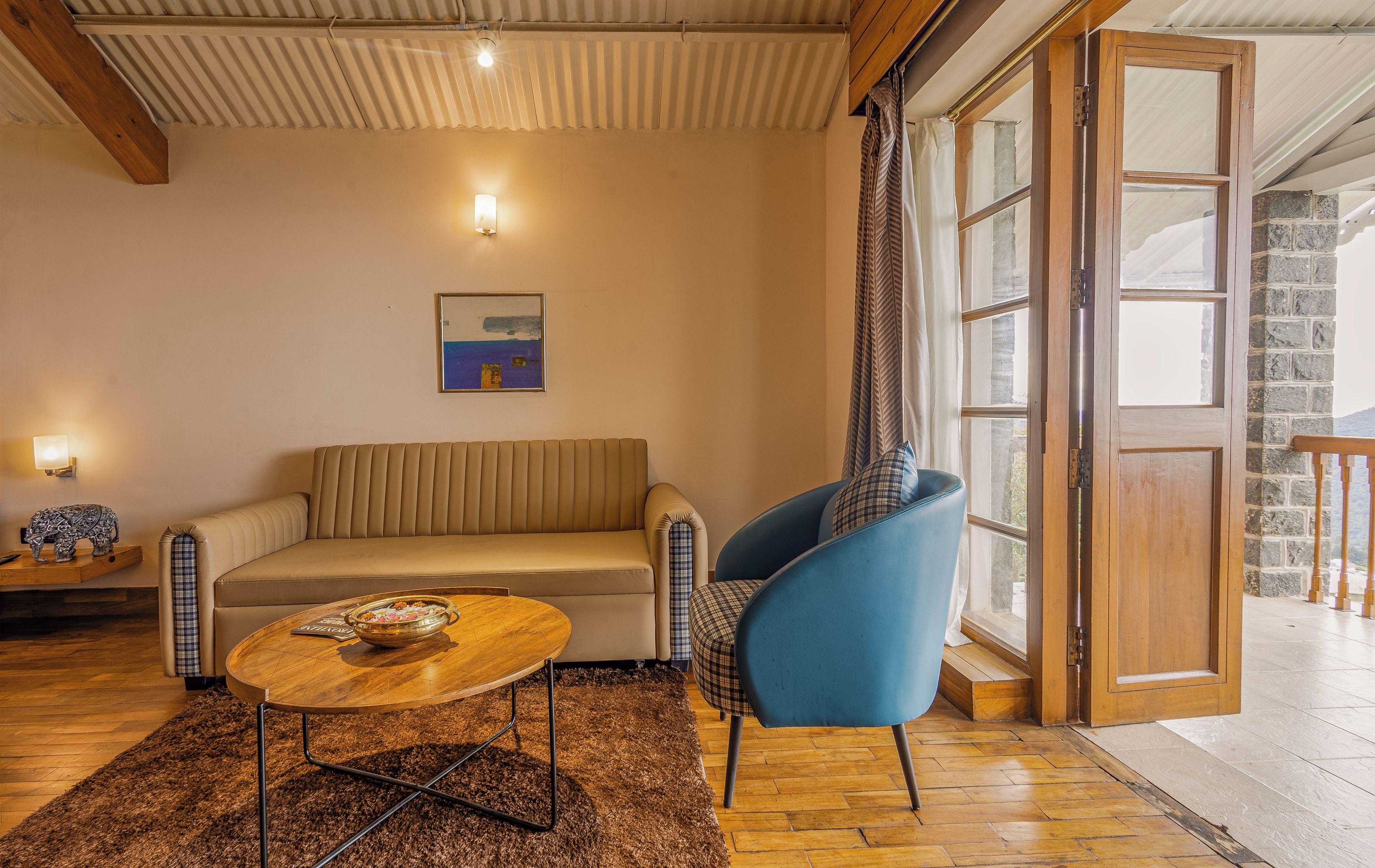 A cozy living room with a sofa, a blue armchair, a wooden coffee table, and a painting on the wall.