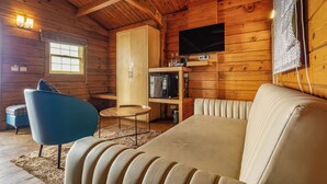 L'intérieur d'une cabane en rondins, avec un canapé, un fauteuil bleu, un téléviseur et un meuble en bois.