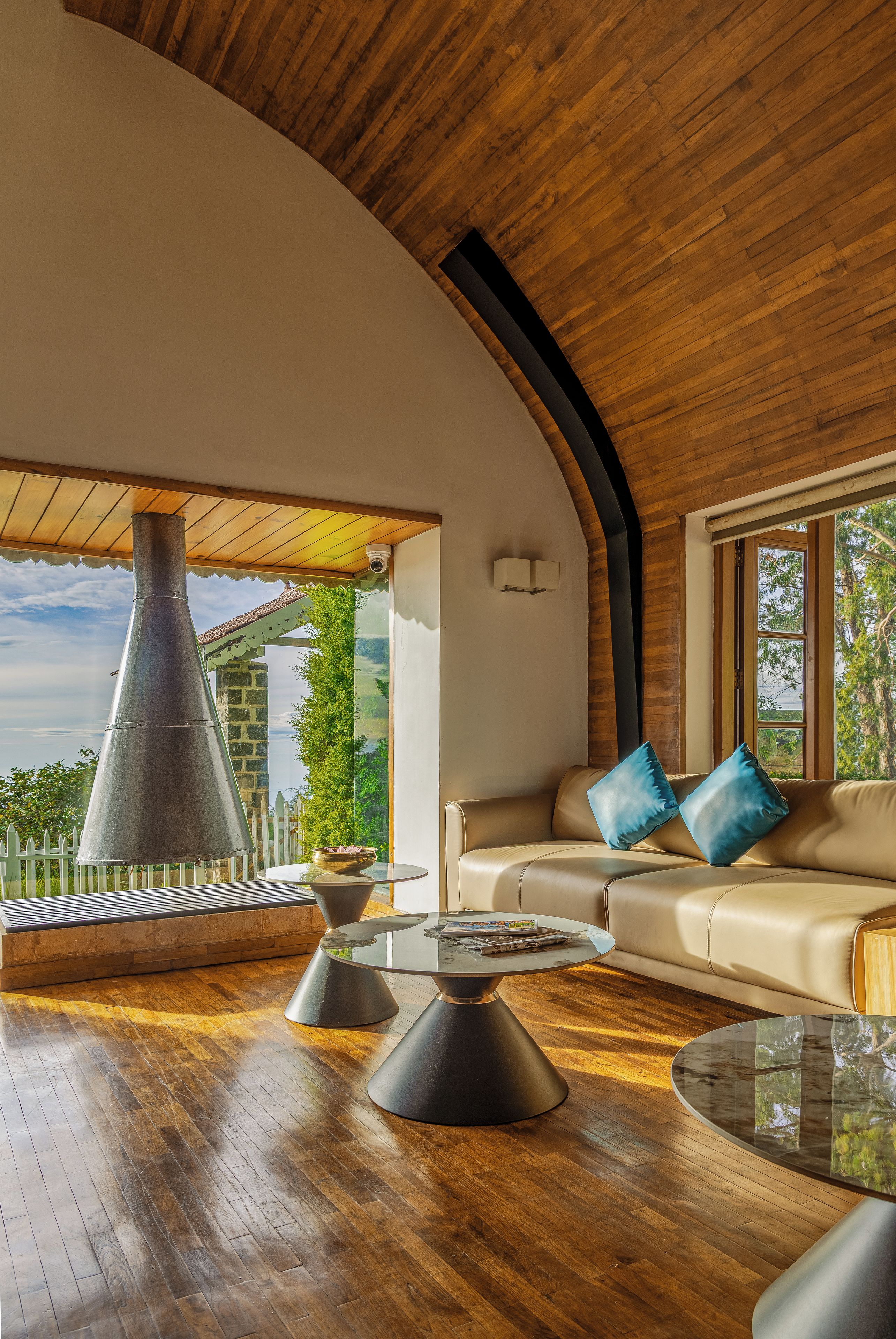 A modern interior with a curved ceiling, a sofa with blue cushions, and a round glass table.