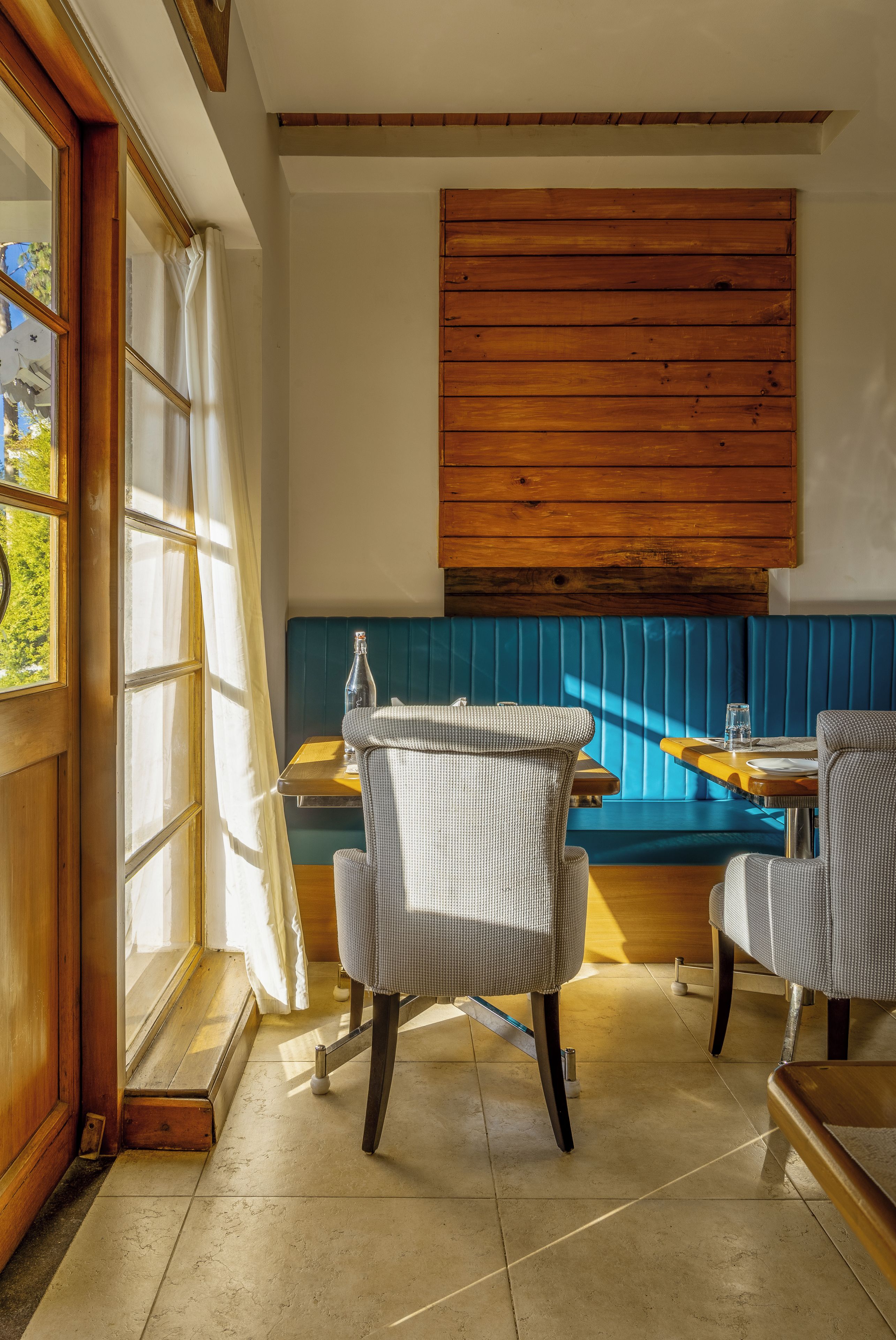 Un comedor con paneles de madera, un banco acolchado azul y dos sillones tapizados.