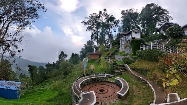 Una escalera de caracol rodeada de exuberante vegetación y un edificio de piedra con tejado metálico.