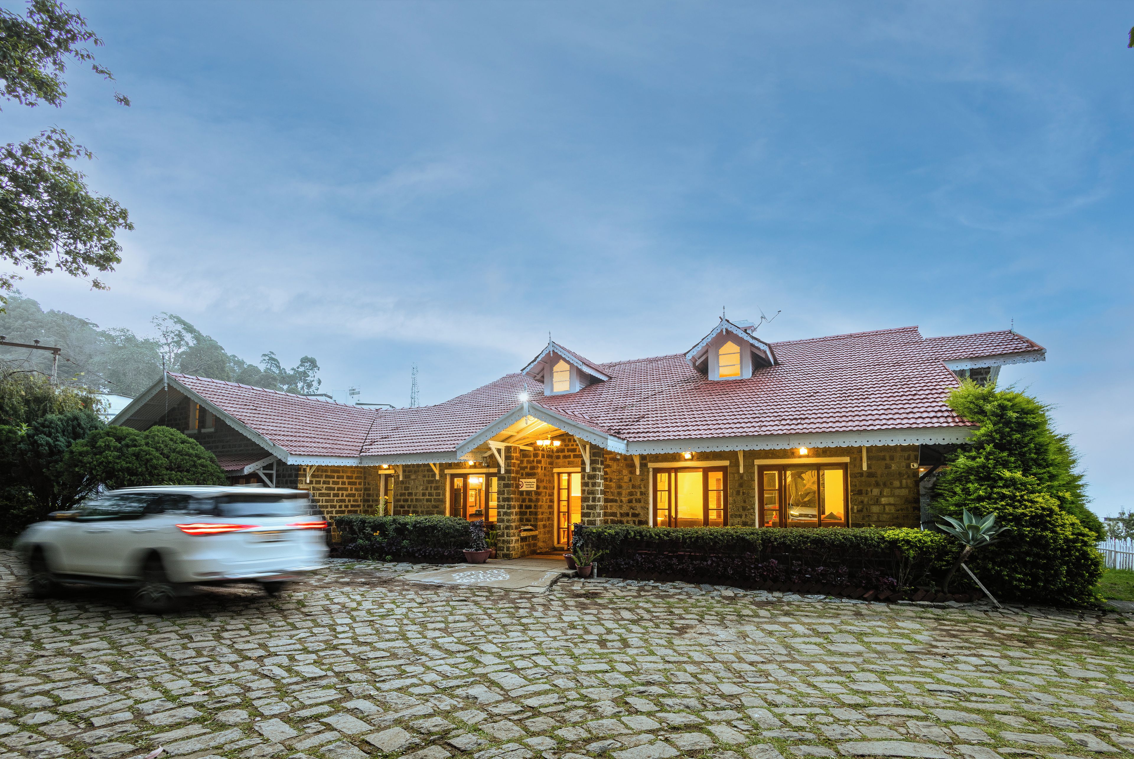 A stone building with a tiled roof, a paved driveway, and a well-maintained garden.
