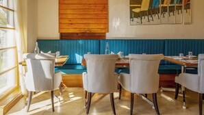 L’intérieur d’un restaurant présente un lambris en bois, un coin salon avec des banquettes bleues et une table à manger avec des chaises.