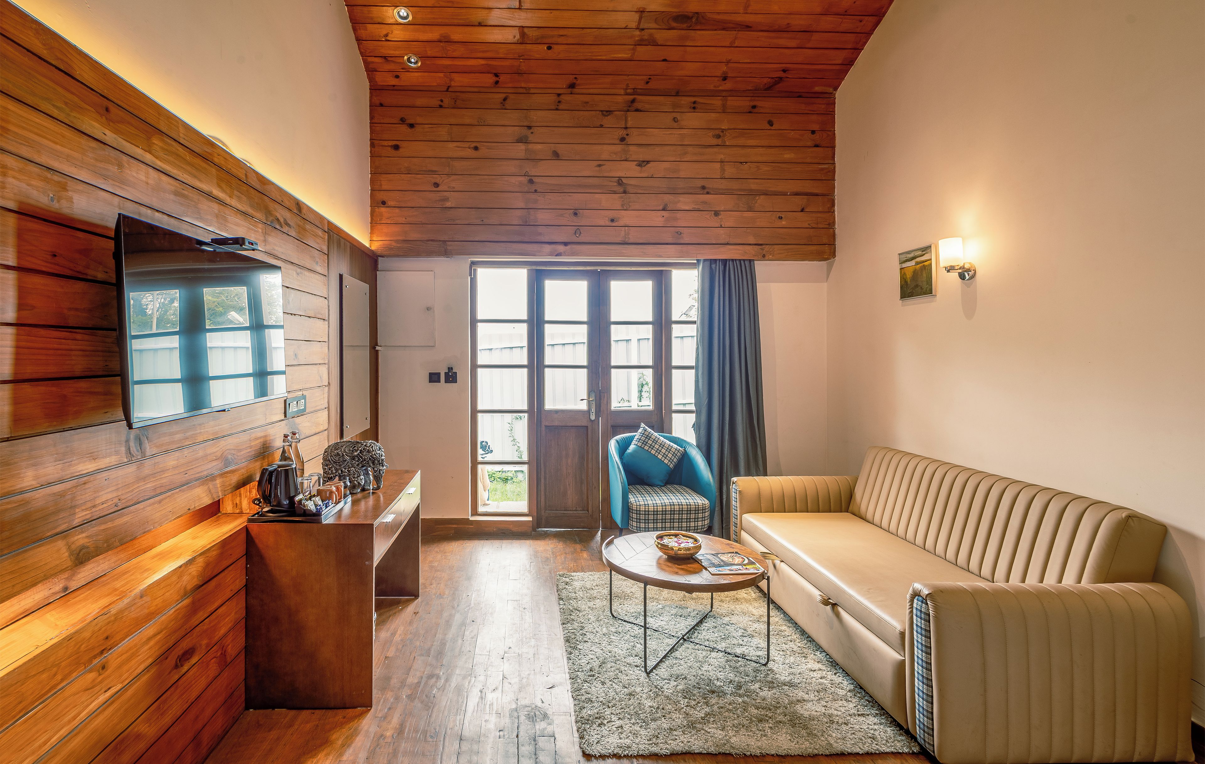 Un salon chaleureux avec un plafond en bois, un canapé, une table basse et un téléviseur fixé au mur.