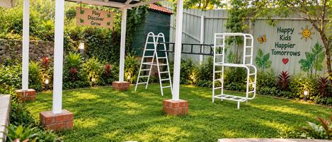 A garden with a play structure, a pergola, and a wall with motivational text.