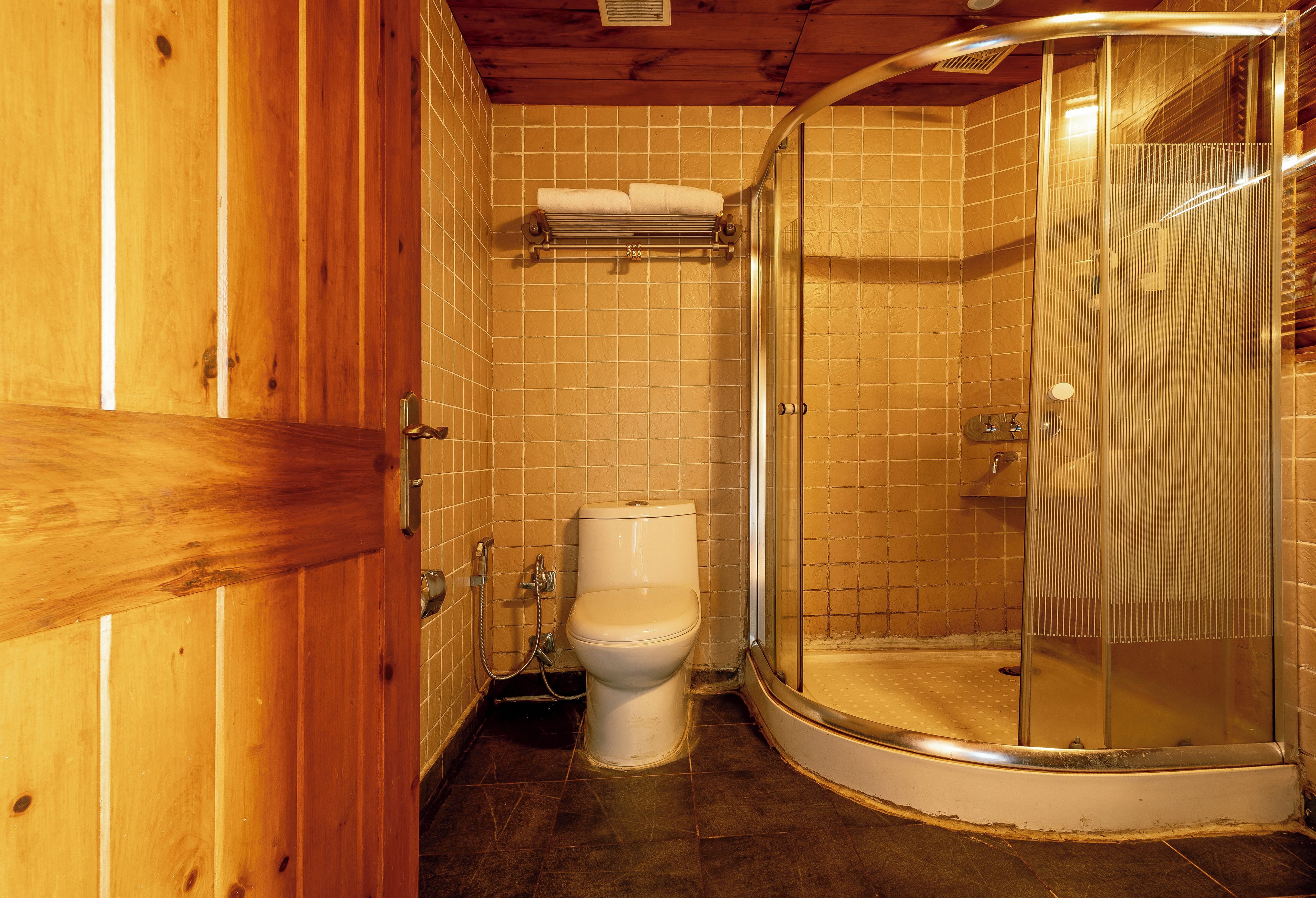 Un baño de madera con inodoro blanco, cabina de ducha y un perchero para toallas.