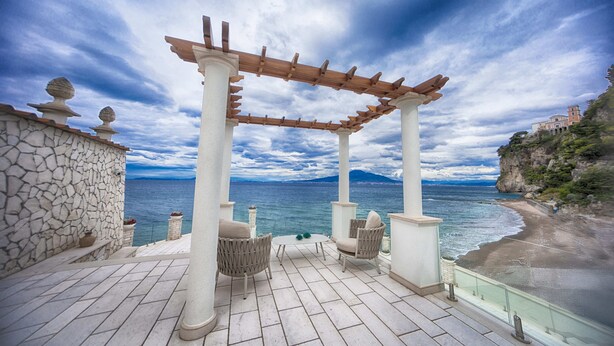 Een terras met een pergola, een stenen muur en uitzicht op zee.
