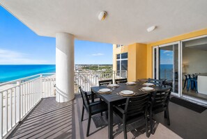 A balcony with a table set for four, overlooking a beach and cityscape. - Seaside Serenity/Corner Unit/Best Gulf View (Panama City Beach)
