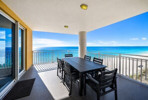 A balcony with a table and chairs, overlooking a beach. - Seaside Serenity/Corner Unit/Best Gulf View (Panama City Beach)