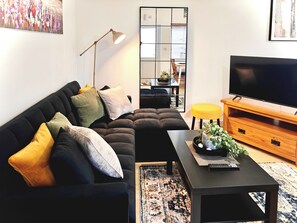 Ein modernes Wohnzimmer mit einem schwarzen Sofa, einem Holz-TV-Schrank, einer Stehlampe und einem großen Spiegel.