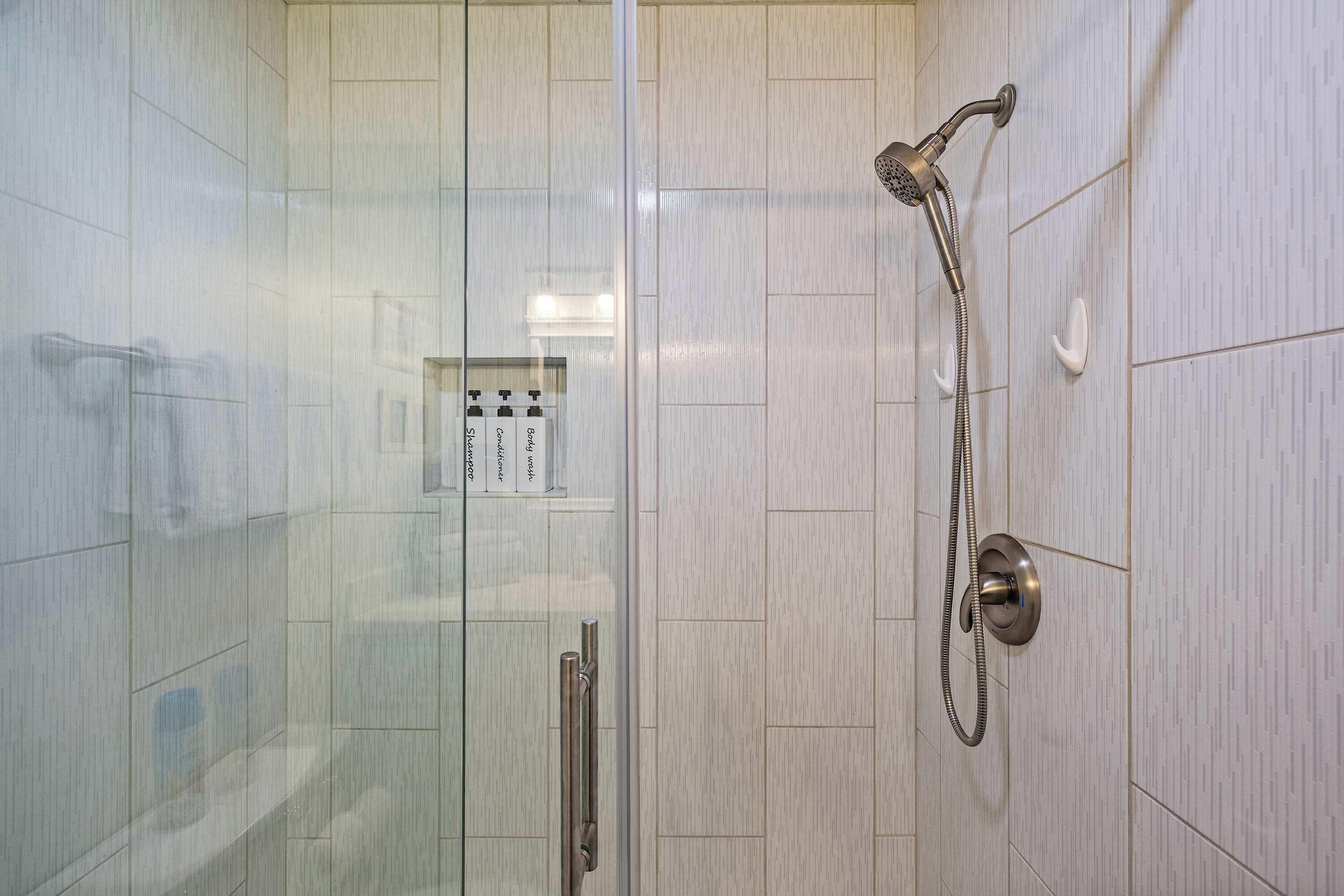 Une douche équipée d’un pommeau de douche à main et d’un robinet mural, d’une porte en verre et d’un panneau de commande avec des boutons.