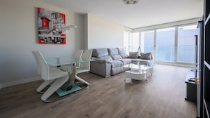 Una sala de estar moderna con una mesa de comedor de vidrio, un sofá gris y un sillón blanco.