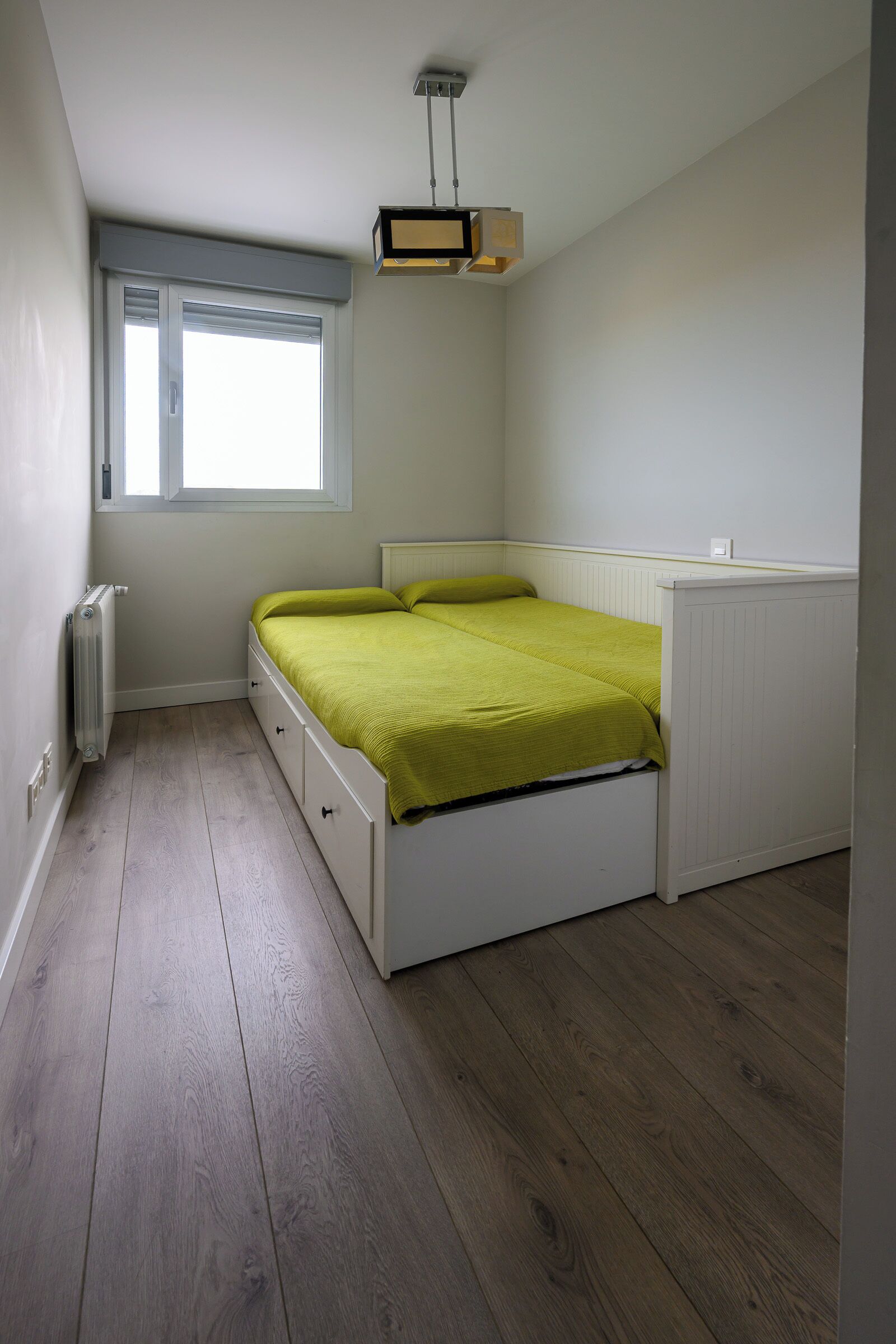 Un dormitorio con cama, radiador, ventana y lámpara.