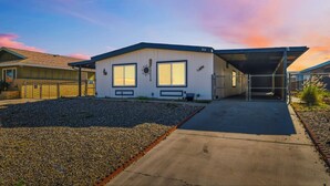 Ein Bungalow mit überdachter Garage, einem Schotterweg und blauem Himmel.