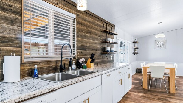 Eine moderne Küche mit einer Wand aus Holzpaneelen, weißen Schränken, einer Arbeitsplatte aus Granit und einem Essbereich mit weißem Tisch und Stühlen.