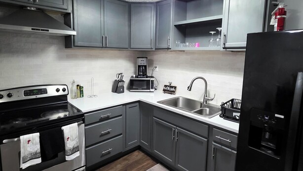 Una cucina moderna con mobili grigi, una cappa in acciaio inossidabile, un forno a microonde, una macchina da caffè, un lavandino e un frigorifero.