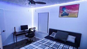 Una camera da letto con un letto, una scrivania, una sedia, una ventola a soffitto e un televisore a parete.