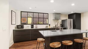 Una cocina moderna con una isla central, taburetes de bar, un ventanal grande y electrodomésticos integrados.