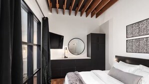 Un dormitorio moderno con un ventanal grande, un espejo redondo, un televisor de pantalla plana y una cama con ropa de cama blanca.