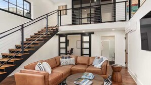 Un amplio salón con un sofá de cuero tipo seccional, una mesa de centro y una escalera que conduce a un nivel superior.