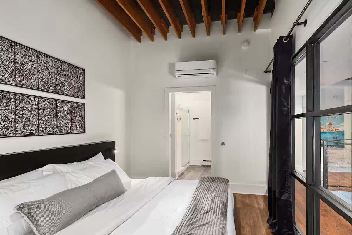 Ein modernes Hotelzimmer mit einem großen Bett, einem Deckenventilator, einem Fenster mit Vorhängen und Blick auf ein Gebäude.