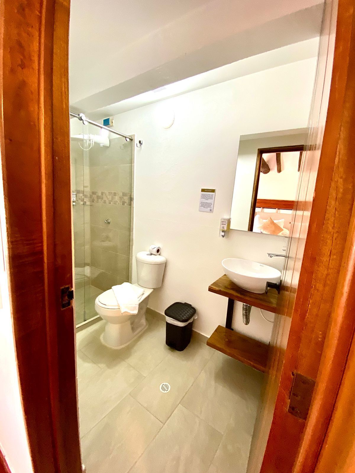 A bathroom with a glass shower enclosure, a toilet, a bidet, a sink, and a trash bin.