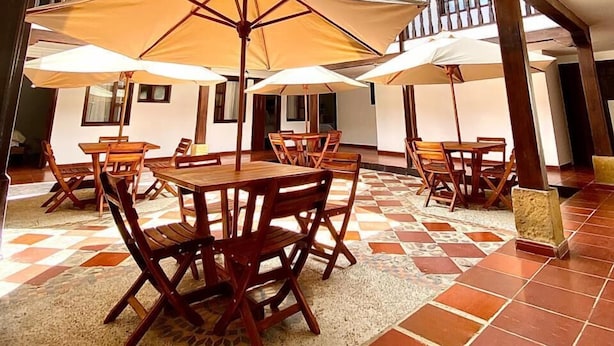 Patio esterno con tavoli e sedie di legno, grandi ombrelloni e vista sul cielo attraverso un lucernario.