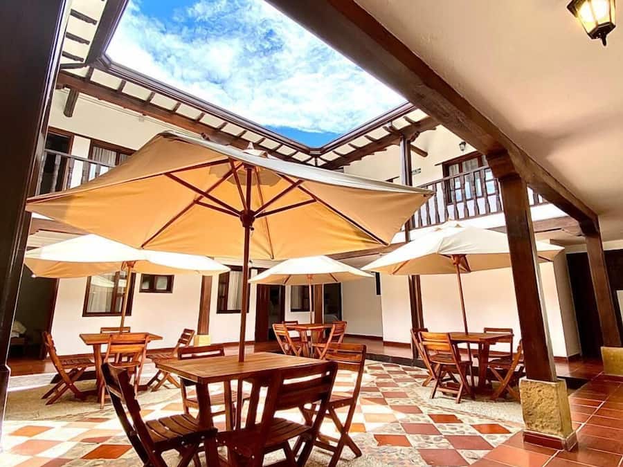 Un patio exterior con mesas y sillas de madera, sombrillas grandes y vistas al cielo a través de un tragaluz.