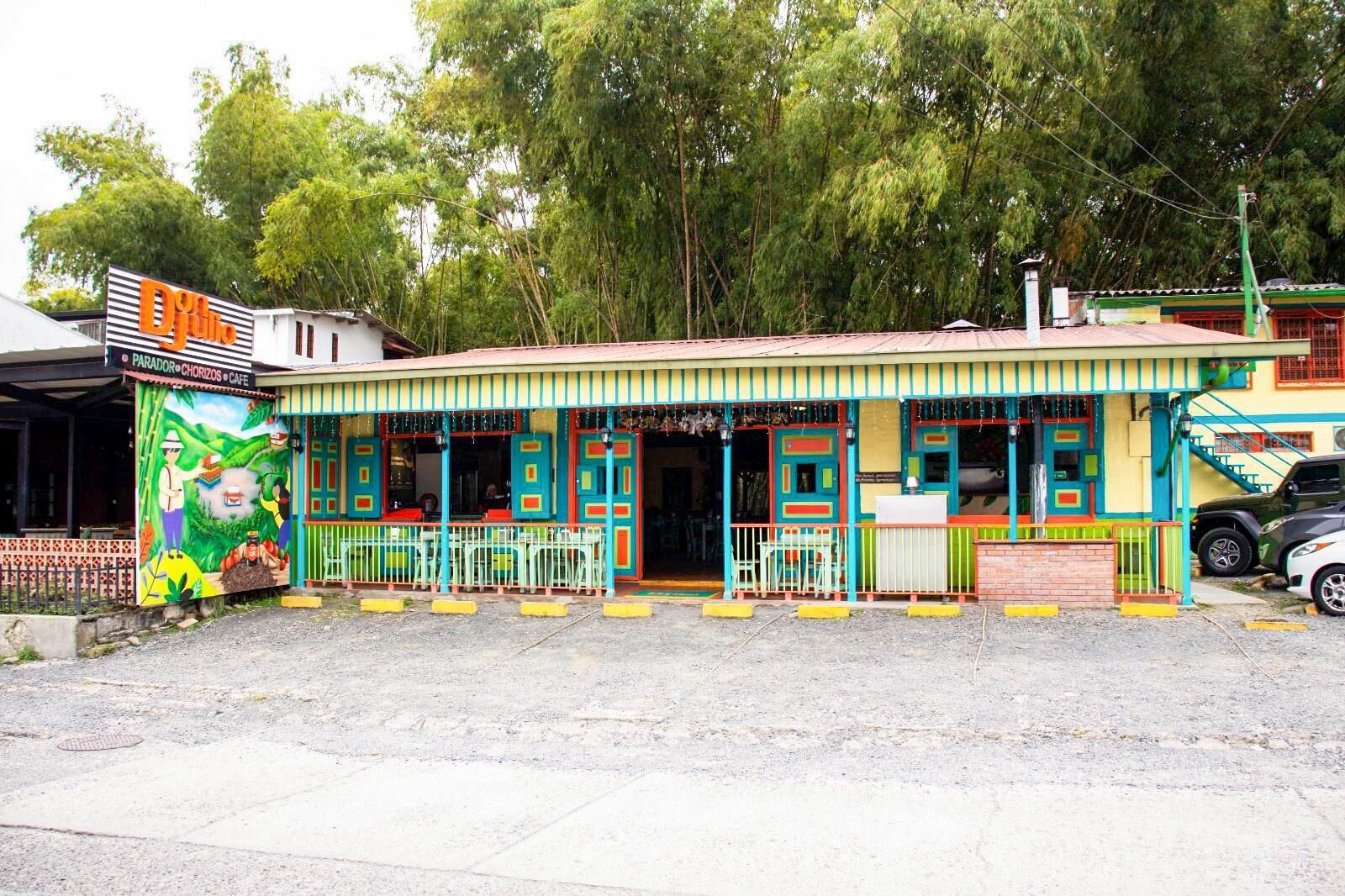 Un edificio colorido con un mural a la izquierda, un área de estar techada al aire libre y una escalera que lleva a la entrada.