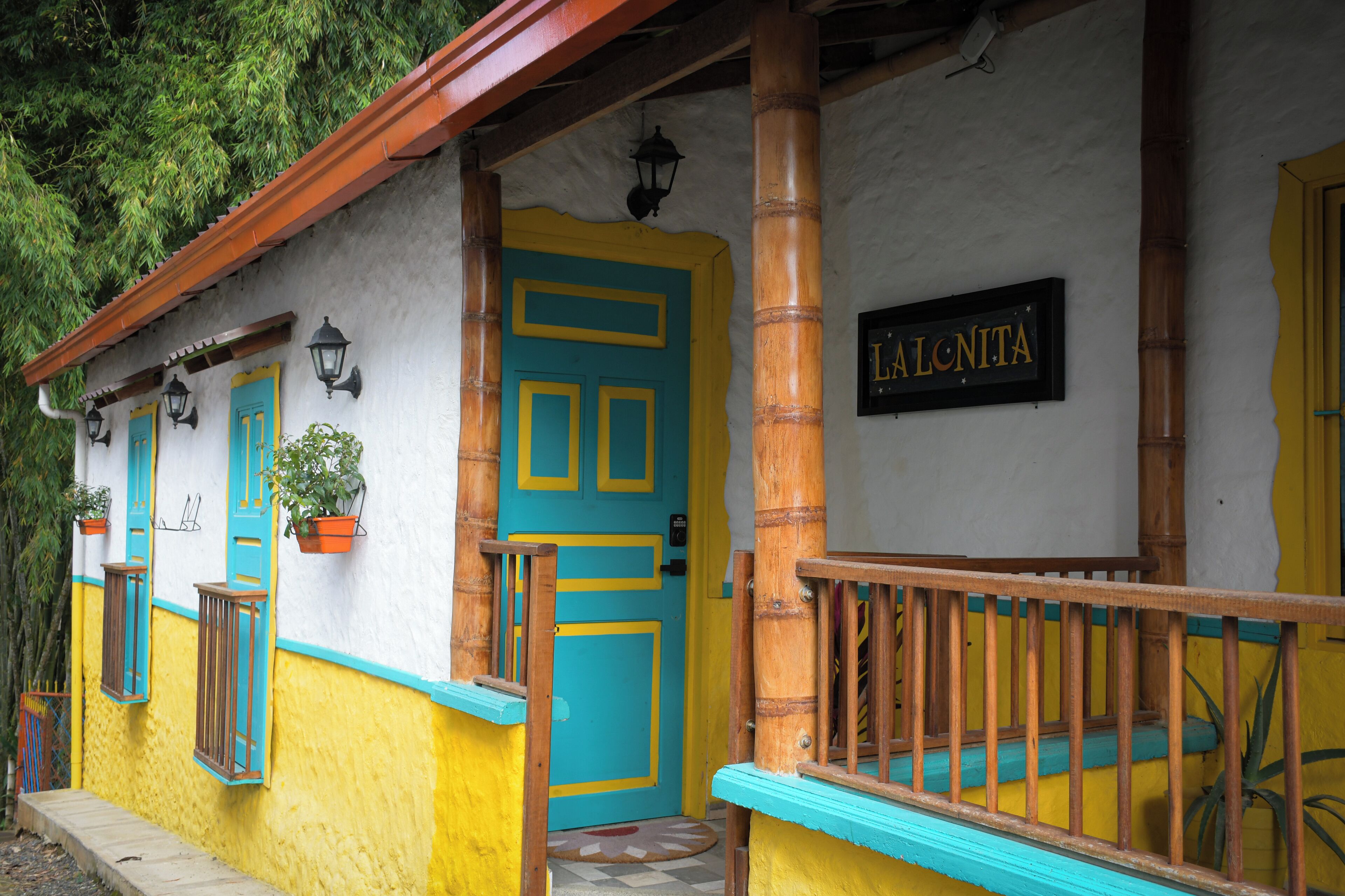 Un edificio con una facciata gialloblu vivace, un portico in legno con ringhiera e una porta con la scritta "LALONITA".