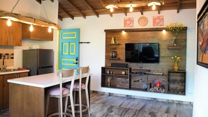 Eine Küche mit Holzausstattung, einer blauen Tür, einer Bar mit Hockern, einem an einer Holzwand montierten Fernseher und einem Kamin mit Blumenvase.