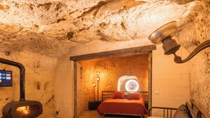 Una habitación tipo cueva con cama, chimenea y televisor en la pared.