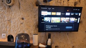 Un televisor montado en una pared texturizada mostrando la interfaz de un servicio de transmisión con opciones como Netflix y YouTube.