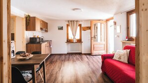 A compact kitchen with wooden cabinets, a dining table, and a red sofa.